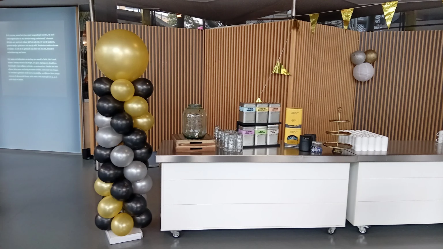 Ballonpilaar in zwart, goud en zilver naast een verzorgde cateringopstelling