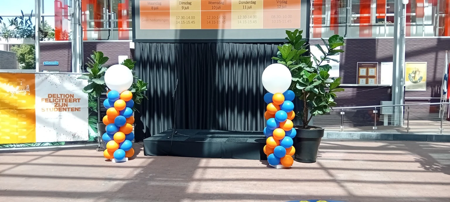 Twee ballonpilaren in blauw en oranje naast een podium